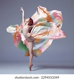 Tender soul. Young classical dancer wearing colorful flying dress dancing on fingertips over grey studio background. Concept of ballet, inspiration, beauty, contemporary dance, creativity, motion, ad - Powered by Shutterstock