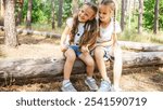 Tender young girls children sit on logs near a pine tree. Kids talk and sincerely communicate, intimacy and openness, trust between sisters. Sibling and childhood relationship concept