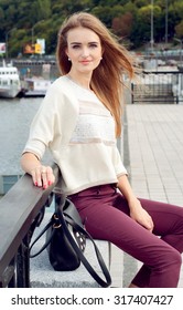 Tender young woman with long blond hair flowing on the wind sitting on the pier and smiling