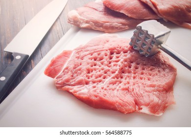 Tenderized piece of raw meat on a white cutting board, with knife and tenderizer - Powered by Shutterstock