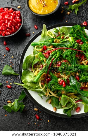 Tenderstem broccoli and egg noodles Asian style vegetarian salad with roasted pine nuts and pomegranate seeds