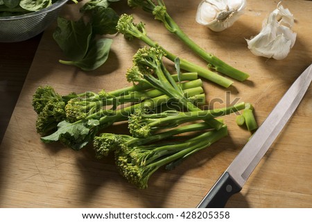 Tenderstem broccoli on a wooden board with a sharp knife and garlic.