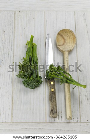 Tender-stem broccoli and utensils on white wooden surface