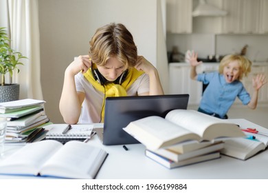 Tennager Boy Study At Home And His Younger Brother Screams And Interrupts Him. Online Education And Distance Learning For High School Students. School Boy Doing His Homework Using Gadgets.