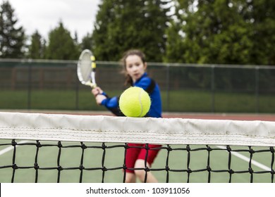 Tennis ball barely clearing the net with female player rushing to net
