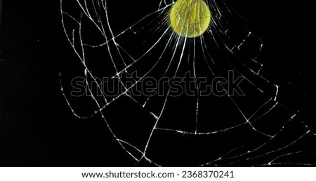 Tennis Ball breaking Pane of Glass against Black Background