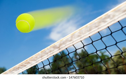 Tennis ball flying fast over a net suggesting a winner point for the match with blue sky