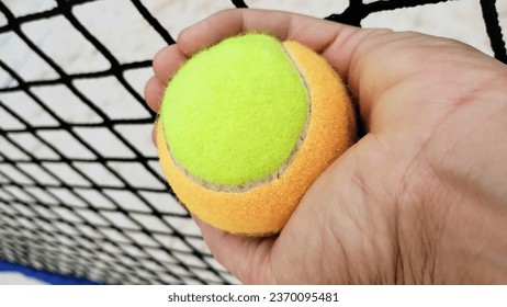 tennis ball in hand and net in the background  - Shutterstock ID 2370095481