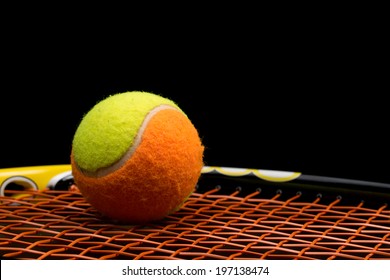 Tennis Ball For Kids With Tennis Racket With Green Grip Handle And Orange Strings On Black Background 