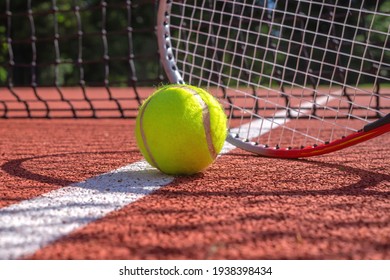 Tennis ball, line and racket on an outdoor court with the racket standing on end casting a shadow across the all weather surface - Powered by Shutterstock