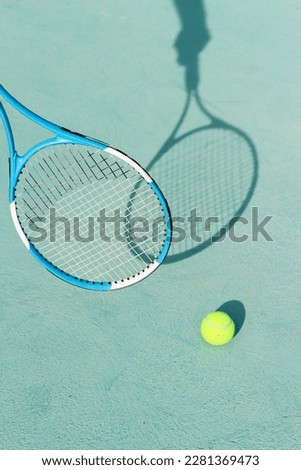 Tennis ball and racket on blue hard tennis court. Shadow of a hand holding tennis racket on the tennis court. Side view, copy space. Summer sport concept. Active lifestyle and healthy living