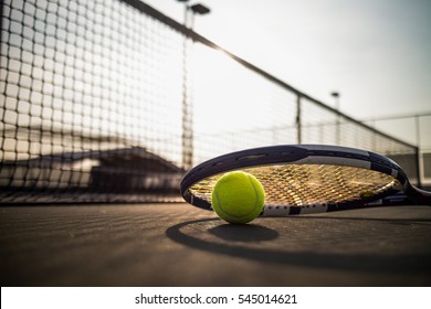 Tennis ball and racket on hard court under sunlight