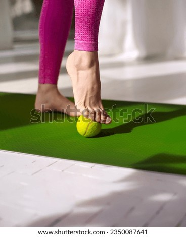Tennis ball roll massage for feet. Woman practicing foot self-massage with a tennis ball. Physiotherapy, reflexology. Tension relieving in the plantar fascia. Improving foot joint mobility.