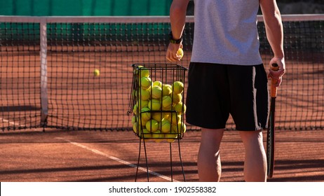 Tennis coach conducts training on red clay court, basket with tennis balls near him. Blurred background. Sports activity and leisure concept. Lifestyle - Powered by Shutterstock