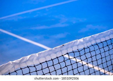 Tennis court net in sports venue with blue playing surface. A view across the net into opposing forecourt.