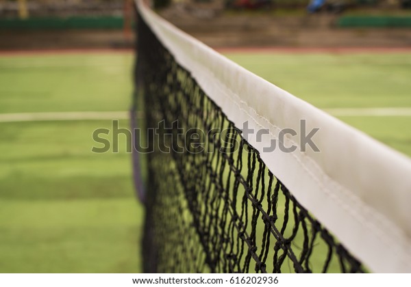 Tennis court net in warm sunlight. Tennis court\
divider. Opposite sites of competitors on tennis court. Summer day\
in tennis club. Outdoor sport and active lifestyle concept. Green\
field for game