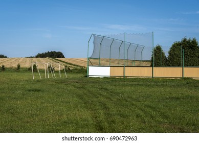 Tennis court and two gates on a green field near the small village in summer