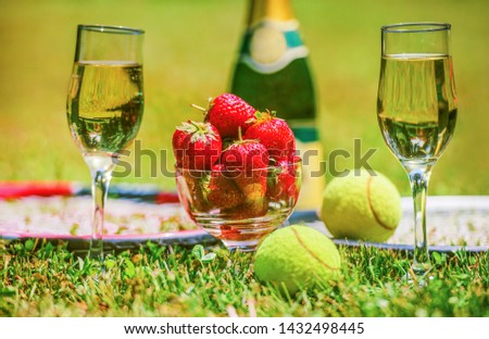 Tennis game. Strawberries, champagne and tennis balls with rackets on the green grass. Sport, recreation concept