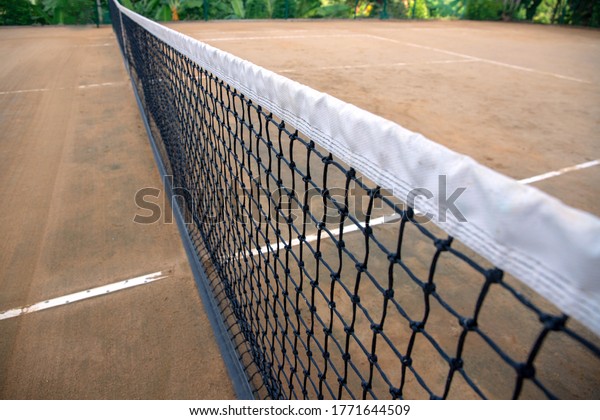 Tennis net on clay court. Black and white net of\
tennis court closeup. Sport field divider. Sport competitors\
opposite sites. Tennis club outdoor. Summer sport and active\
lifestyle concept. Grand\
slam