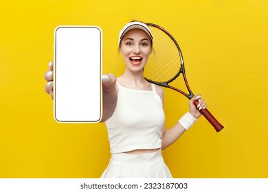 tennis player girl in sportswear holding tennis racket and showing blank screen of smartphone on yellow isolated background, female tennis coach in white uniform advertises copy space on phone display - Powered by Shutterstock