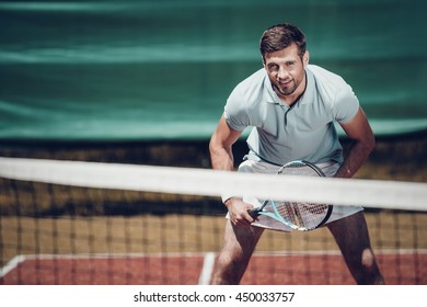 Tennis player. Handsome young man in polo shirt holding tennis racket and smiling while standing on tennis court - Powered by Shutterstock