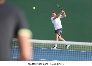 Tennis Player Man Hitting Backhand Returning Ball With Racket On Green Background. Sports Men Playing Together On Outdoor Court.