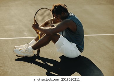 Tennis player sitting and resting with a racket on a court in sportswear outdoors during daytime. Reflecting fatigue and determination in sports. - Powered by Shutterstock