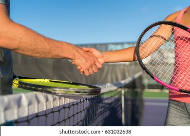 Tennis players shaking hands at court net at end of fun game. Man and woman playing recreational tennis handshaking with tennis racquets.