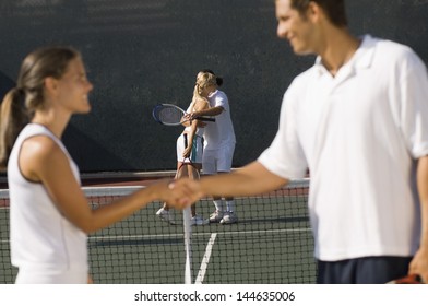 Tennis players shaking hands at net with teammates hugging in background - Powered by Shutterstock