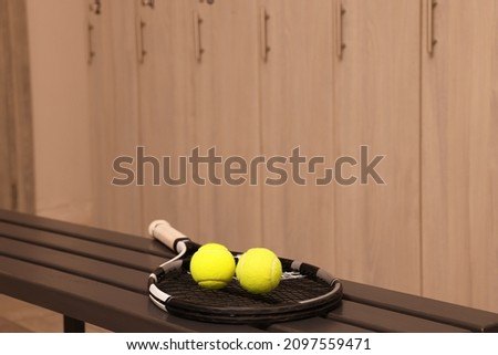 Tennis racket and balls on wooden bench in locker room