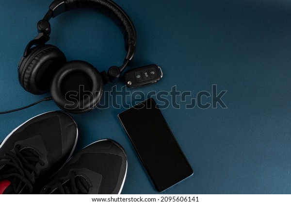 Tennis shoes,\
headphones, cell phone and car keys to go exercise, with blue\
background and space for\
text
