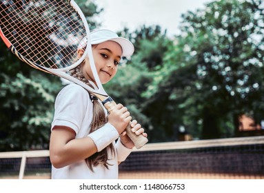Tennis training for young kid outdoors. Portrait of happy sporty little girl on tennis court. Caucasian child in white tennis sportswear on training.