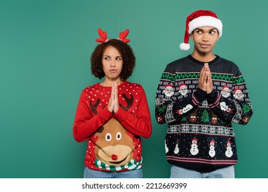 Tense African American Couple In Christmas Outfit Standing With Praying Hands And Looking Away Isolated On Green