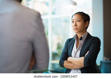 Tense Asian businesswoman looking at male partner with crossed arms. Two colleagues confronting each other in office space. Clashing personalities concept - Shutterstock ID 1204911457