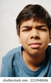 Tense Indian Boy With Closed Eyes Over White Background. Close Up. He Wears Simple Cotton Shirt