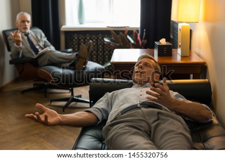 Tense man. Tense Caucasian male patient lying on the couch in front of his psychotherapist while complaining about his problems