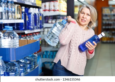 Tense Modern Woman Lifting Heavy Bottle Of Still Water While Shopping At Grocery Store