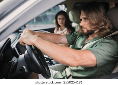 A tense moment in a car, man focusing on the road while woman appears concerned The background shows a blurred outdoor setting - Powered by Shutterstock