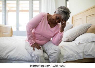 Tense Senior Woman Sitting On Bed In Bedroom At Home