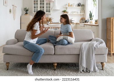 Tense teen girl holding pillow and looking at nervously gesturing mother sits on couch. Annoyed family quarrel between mother woman and daughter due to lack of time or money for mom to together walk. - Shutterstock ID 2223116431