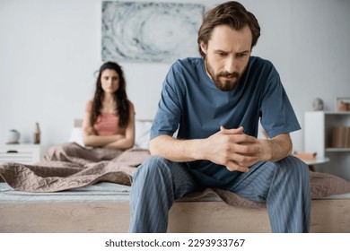 Tensed man in pajama sitting near blurred girlfriend in bedroom at home - Powered by Shutterstock