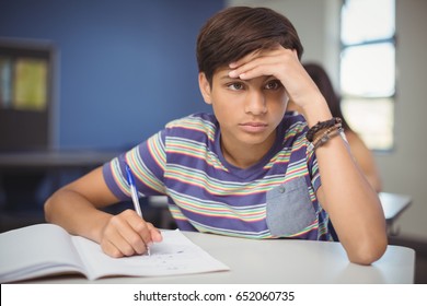 Tensed school boy doing homework in classroom at school - Powered by Shutterstock