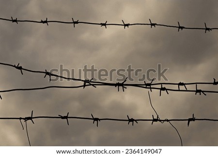 Tensioned barbed wire against a background of thick dark clouds