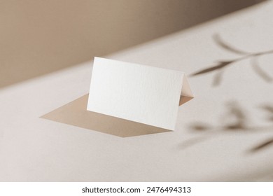 Tent folded white blank name card on minimalist background with plant leaves shadows; place table card mockup template for events and weddings