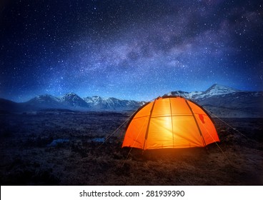A tent glows under a night sky full of stars. 