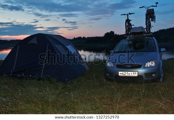 Tent near Volga River. Hike. Car with bikes on\
roof. Staritsa town, Tver region Russia July 2013. Sunset in\
nature. nature landscape camping tent with tree on green grass\
meadow and fog in jungle