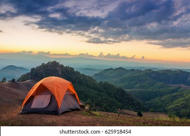 Tent on the hill beneath the mountains under dramatic sky