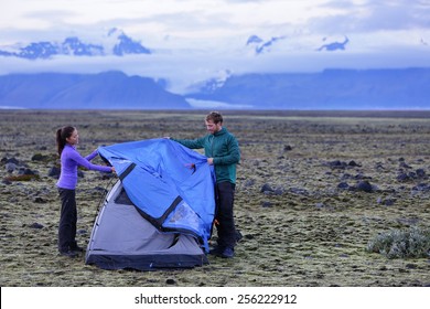 Tent - People Pitching Tent On Iceland At Dusk. Couple Setting Up Camp For Night After Hiking In The Wild Icelandic Nature Landscape. Multicultural Asian Woman And Caucasian Man Healthy Lifestyle.