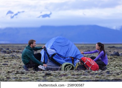 Tent - People Pitching Tent On Iceland At Dusk. Couple Setting Up Camp For Night After Hiking In The Wild Icelandic Nature Landscape. Multicultural Asian Woman And Caucasian Man Healthy Lifestyle.