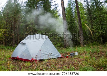 Tent in the wood and the water is boiling in the pot at the gas burner.